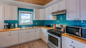 A modern kitchen with white cabinets, a teal backsplash, a gas stove, a microwave, and a window providing natural light.