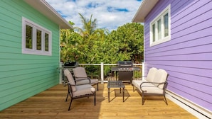 A covered deck with two chairs and a grill, surrounded by a wooden deck and a small fence.