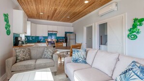A modern apartment with a wooden ceiling, a kitchenette, a dining area, and two sofas with patterned cushions.