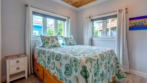 A bedroom with a bed, two windows, a nightstand, and a ceiling fan.