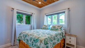 Une chambre à coucher avec un lit en bois, deux fenêtres avec des rideaux, une table de chevet et un ventilateur de plafond.