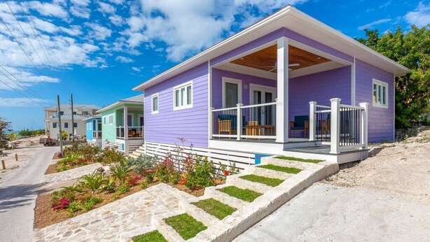 Une maison moderne à deux étages, à l’extérieur violet, dotée d’un porche et d’un jardin aménagé avec des pierres plates qui mènent à l’entrée.
