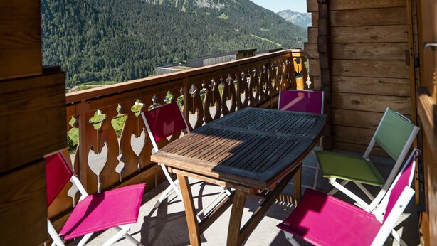 Une terrasse en bois avec une table et des chaises, offrant une vue sur un paysage montagneux.