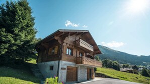 Une maison en bois à deux étages, dotée d’un balcon, située dans un paysage vallonné.