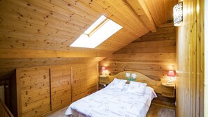 Une chambre confortable dans un chalet en bois, avec une lucarne, un lit recouvert d’une courtepointe à motifs et deux lampes de chevet.