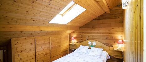 A cozy wooden cabin bedroom with a skylight, a bed with a patterned bedspread, and two bedside lamps.