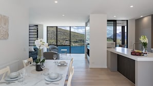 Eine moderne Küche mit Essbereich, große Fenster mit Blick auf eine gebirgige Landschaft und eine kleine Kochinsel mit Obst und Blumen.