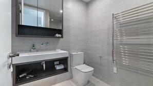 Une salle de bain moderne avec un lavabo blanc, un miroir au-dessus, des toilettes et un porte-serviettes.