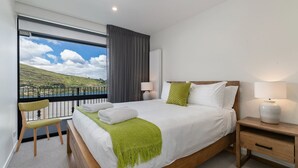Une chambre d’hôtel avec un grand lit, une chaise, une table de chevet et une vue sur un lac et des collines.