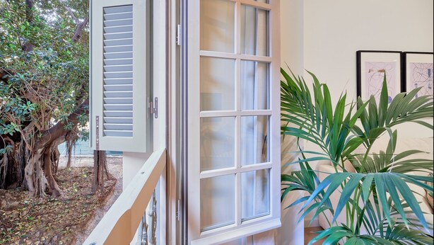 Quarto com uma janela grande, vista para árvores e um vaso de planta.