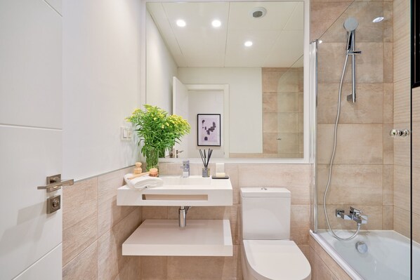 A modern bathroom with a white sink, toilet, and bathtub. There is a showerhead and a mirror above the sink.
