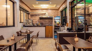 A modern restaurant interior with a kitchen area, dining tables, and chairs. - Imara Hotel (Kampala)