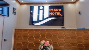 A reception area with a sign for Imara Hotel, a wooden panel wall, and a floral arrangement. - Imara Hotel (Kampala)