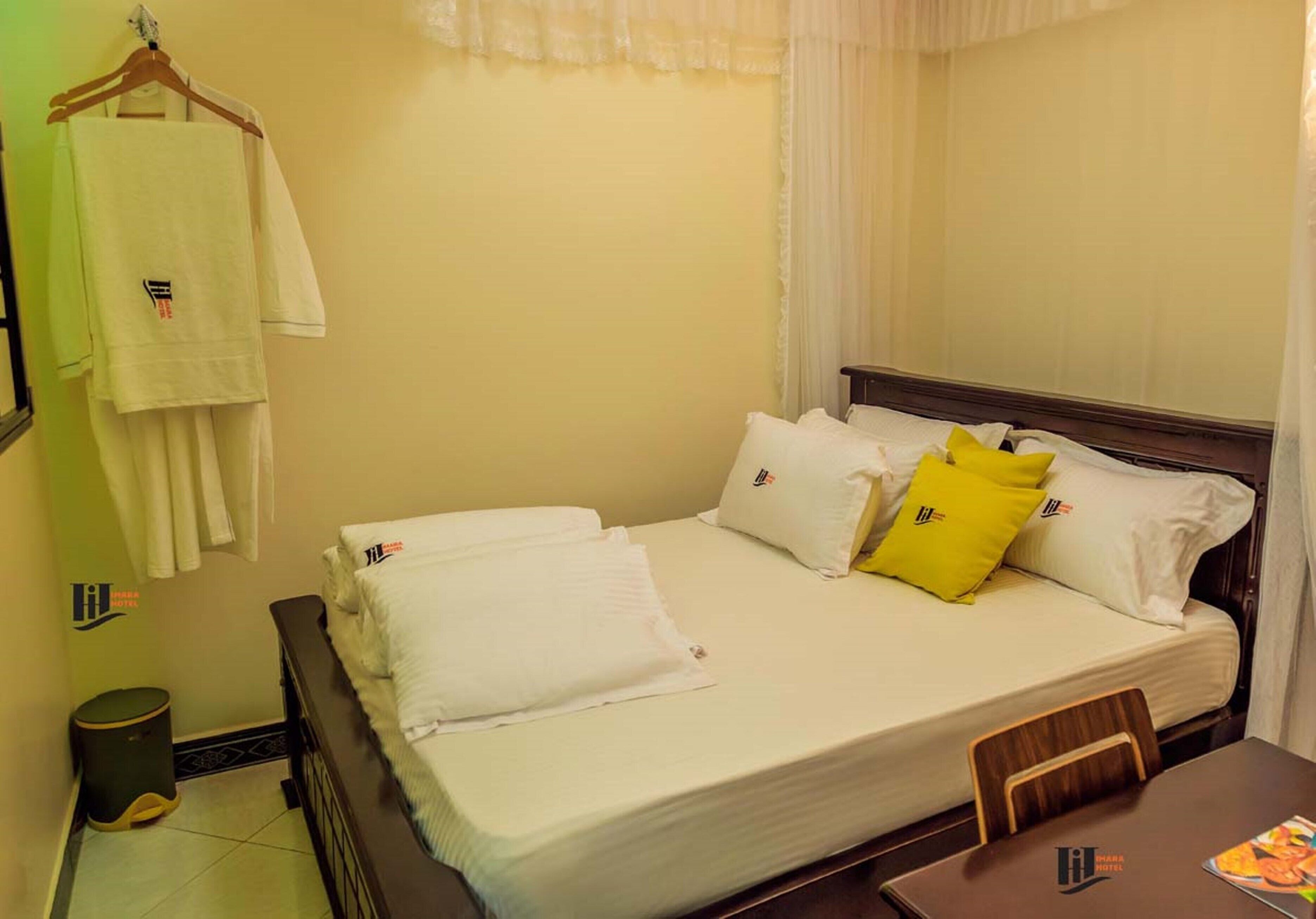 A hotel room with a bed, a chair, a table, and a trash bin.