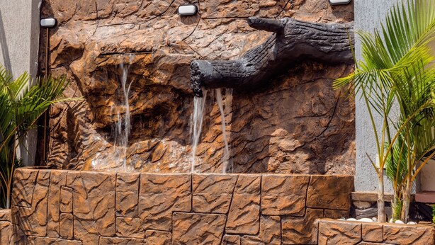 A rock wall with a waterfall feature and palm plants. - Imara Hotel (Kampala)