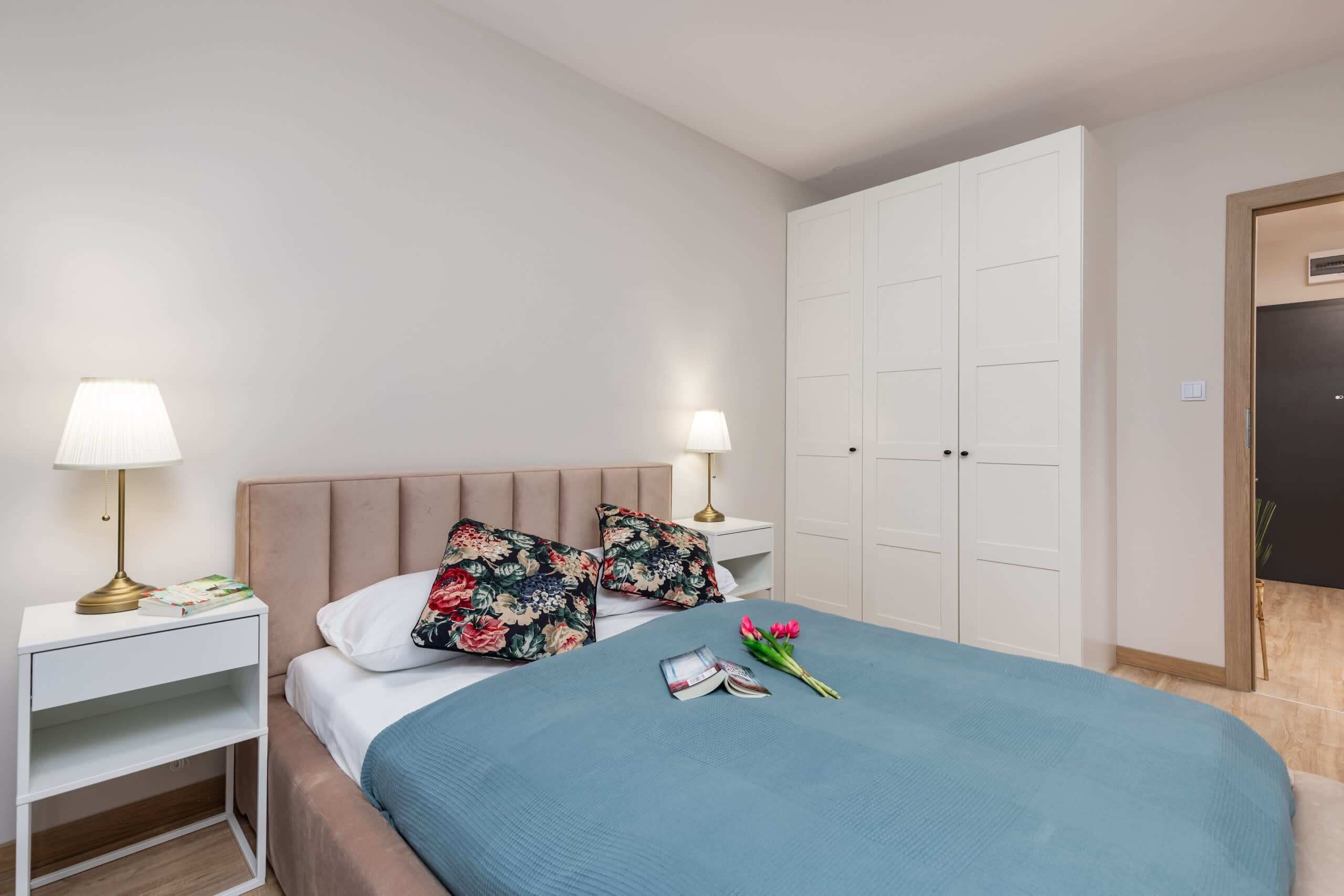 Een netjes ingerichte slaapkamer met een bed, twee nachtkastjes met lampen, een kledingkast en een deur.