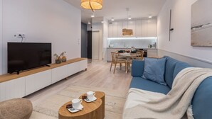Een moderne woonkamer met een flatscreen-tv, een blauwe bank, een houten salontafel en een eethoek met een tafel en stoelen.