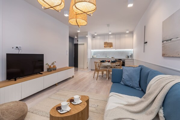 Una sala de estar moderna con un televisor de pantalla plana, un sofá azul, una mesa de centro de madera y una zona de comedor con una mesa y sillas.
