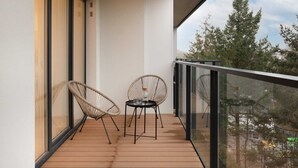 Een balkon met twee rieten stoelen en een kleine tafel, met uitzicht op een bebost gebied.