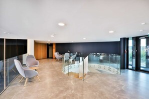 En modern entréhall med böjda glasväggar, sittgrupper och utsikt över utomhusmiljön genom glaset.