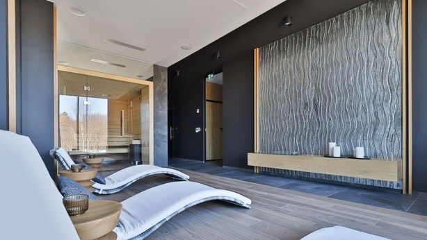 Ein moderner Wellnessbereich mit einer Rezeption, Massagesesseln und einer strukturierten Wand.