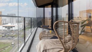 Ein Balkon mit Korbstühlen, einem kleinen runden Tisch und einem Glas Orangensaft, mit Blick auf die Stadt.