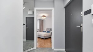 Ein schmaler Flur, der zu einem Schlafzimmer mit Bett, Deckenleuchte und Tür führt.