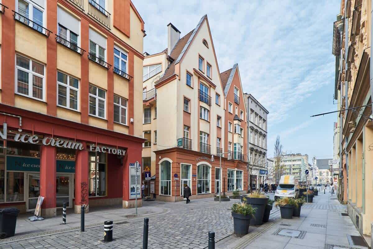 Une rue pavée bordée de bâtiments historiques, dont un magasin dont l’enseigne indique clairement qu’il s’agit d’une « usine de glaces ».