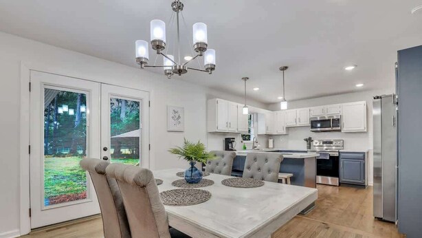 A modern kitchen with white cabinets, stainless steel appliances, and a dining area with a white table and chairs. - Restful Haven Near Savannah - King Bed (Pooler)