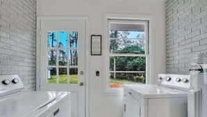 A laundry room with white appliances, a door with a window, and a view of trees. - Restful Haven Near Savannah - King Bed (Pooler)