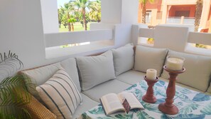 Um espaço de estar aconchegante com um sofá, almofadas, uma mesa com um livro e velas.