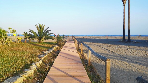 A wooden boardwalk leading to a beach with palm trees and a clear sky. - Comfort and exclusivity on the tropical coast (Motril)