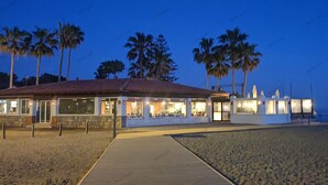 A beachfront building with a thatched roof, large windows, and a paved walkway leading to the entrance. - Comfort and exclusivity on the tropical coast (Motril)