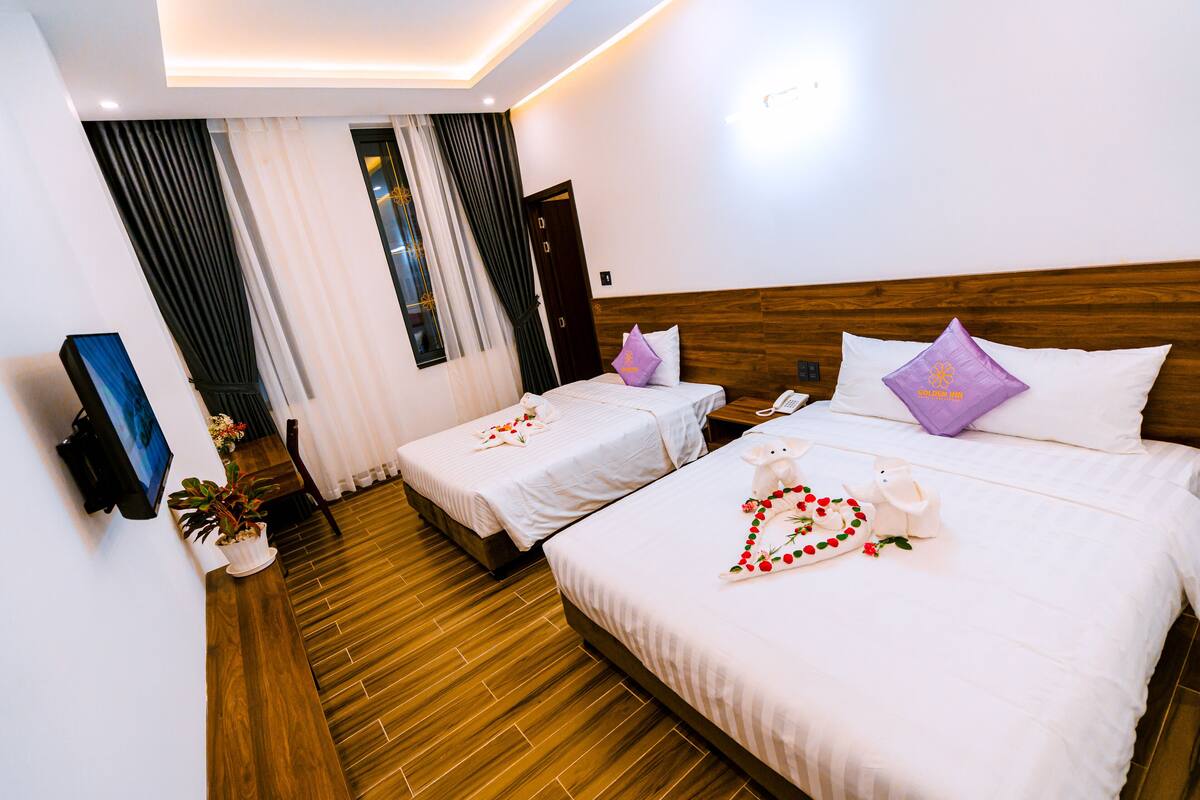 A hotel room with two beds, wooden flooring, white bedding, and a small potted plant.