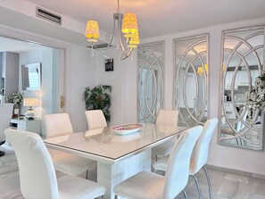 A modern dining area with a glass table, white chairs, and a chandelier.