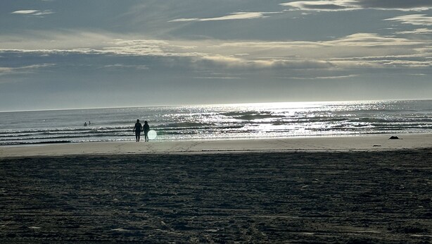 Een strandscène met de zon die schijnt en twee mensen die over het zand lopen.