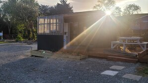 Een klein gebouw met een metalen gevel en een glazen deur, gelegen op een grindpad met bomen op de achtergrond.