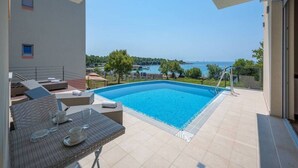 Zona de piscina en la azotea con vistas despejadas al mar, mesa de comedor con sillas y un área de estar con sofás.