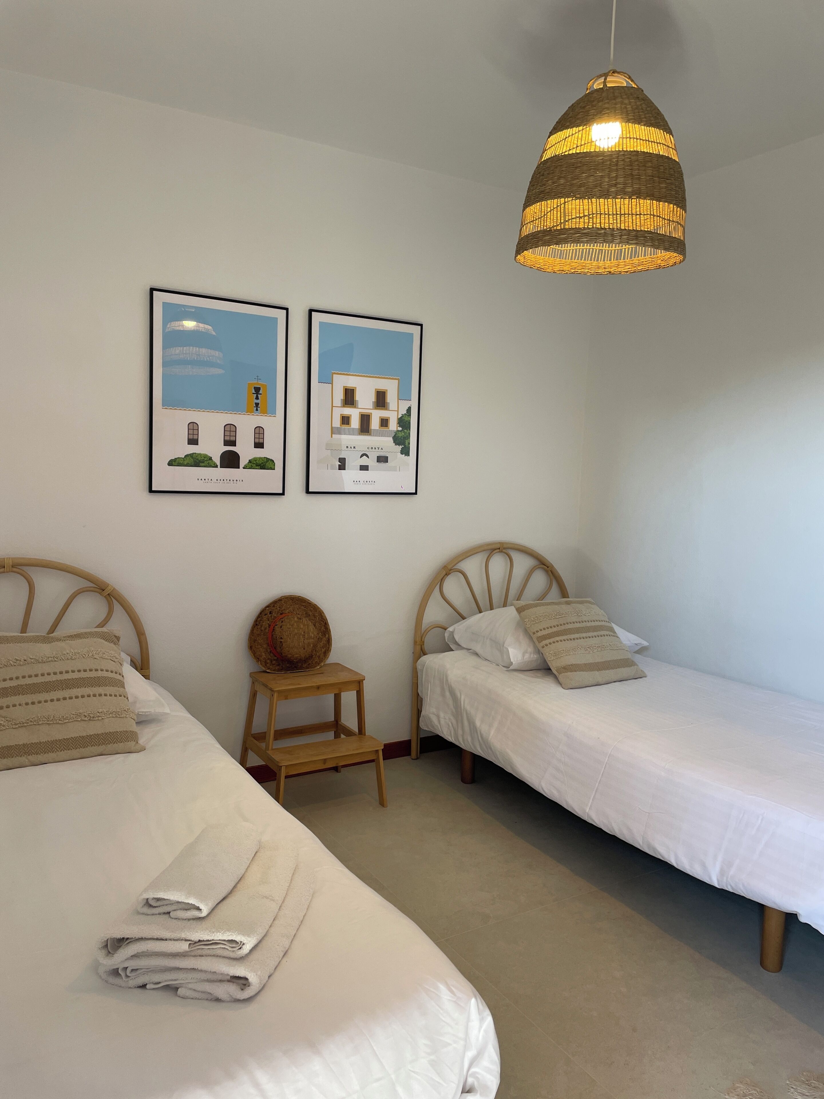 A bedroom with two single beds, a hanging light fixture, and two framed pictures on the wall.