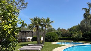A pool area with lounge chairs, a covered seating area, and a well-maintained lawn.