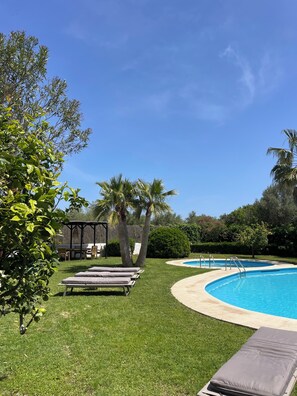 Ein Poolbereich mit Liegestühlen, einer überdachten Sitzgelegenheit und einem gepflegten Rasen.