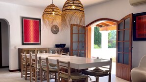 A dining area with a long table, wooden chairs, and two hanging wicker chandeliers.