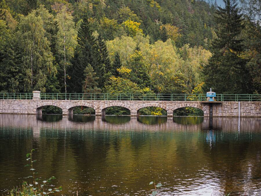 Uma ponte de pedra sobre águas calmas, rodeada por vegetação exuberante e árvores.