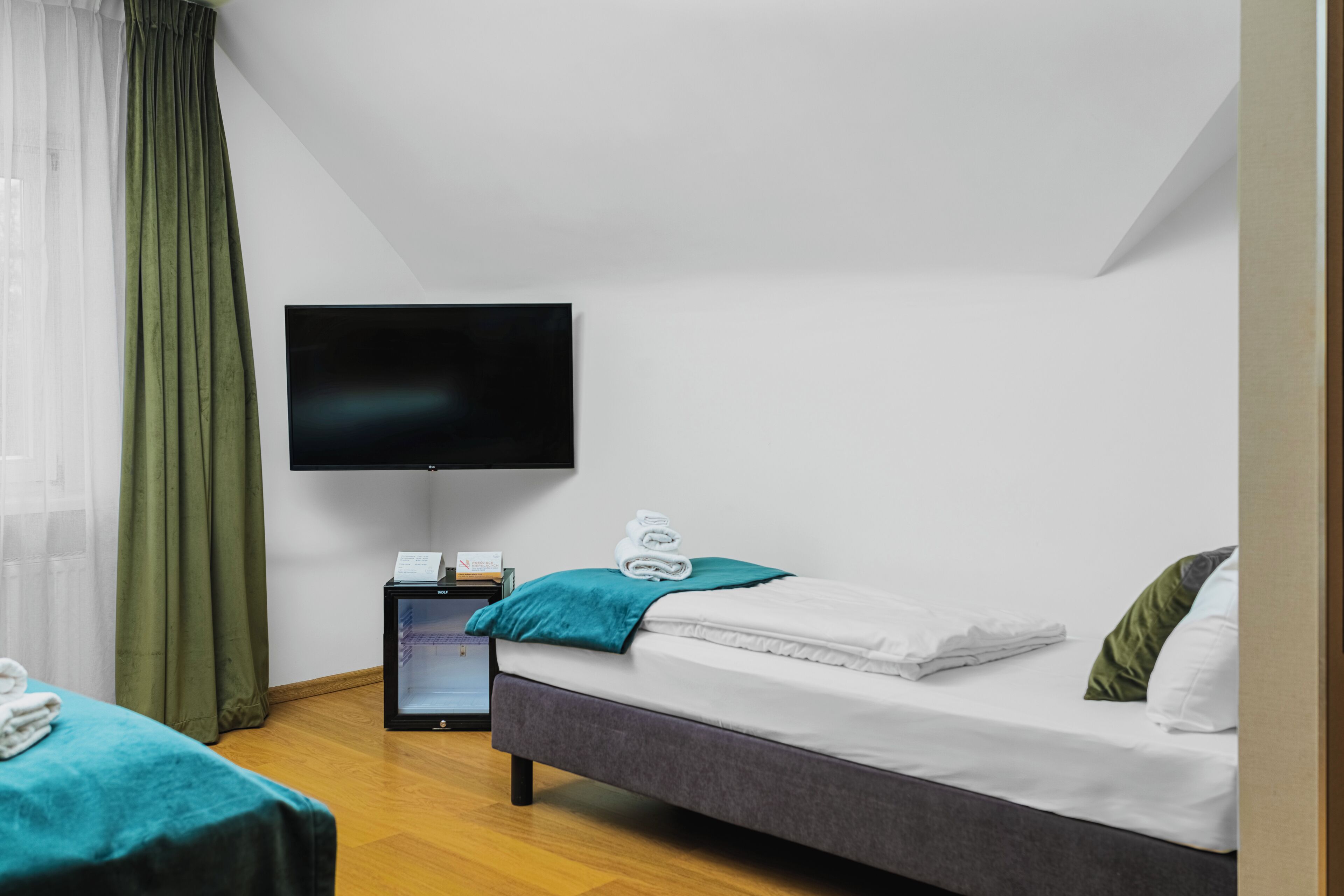 A hotel room with two beds, a flat-screen TV, a minibar, and a window with curtains.