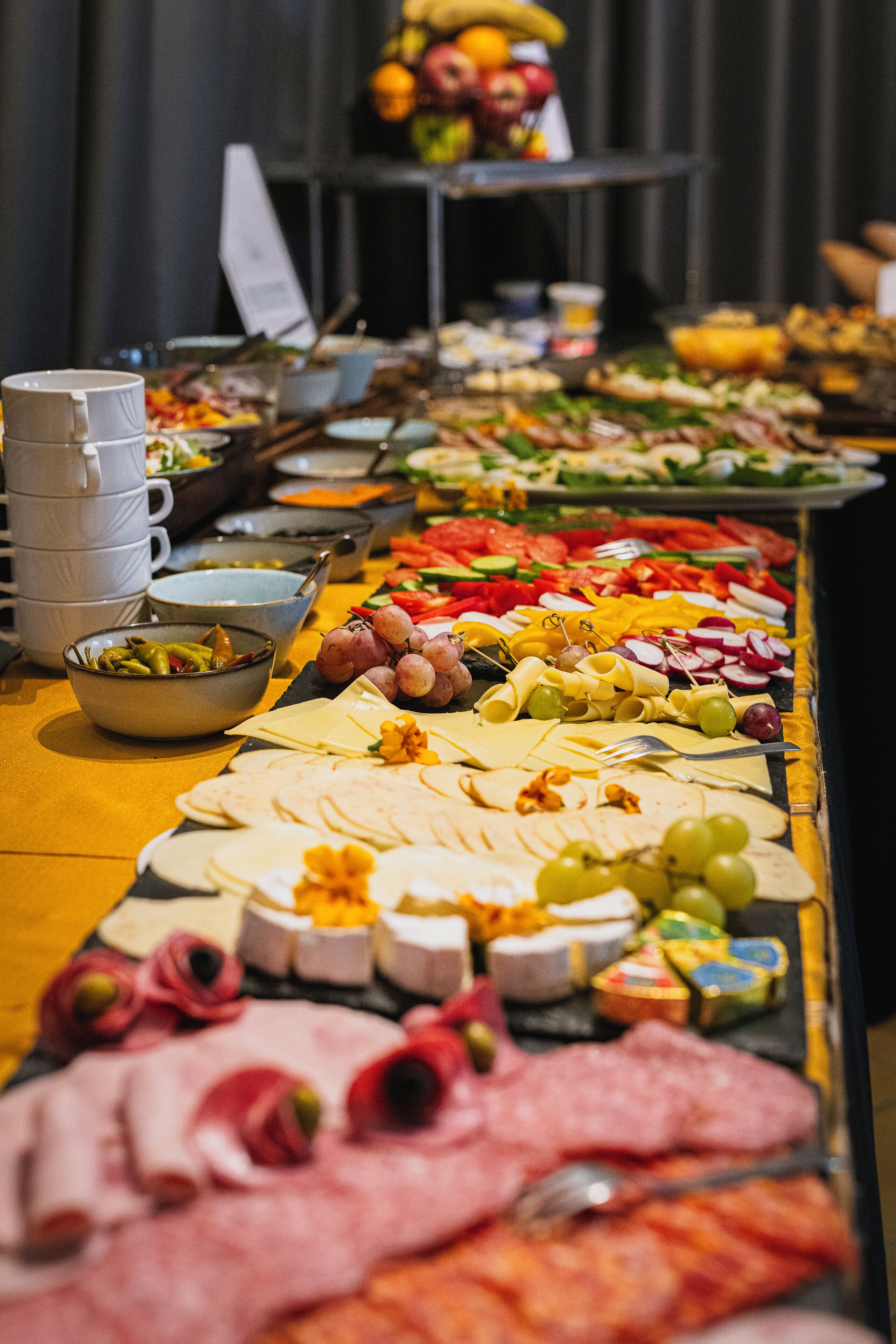 A buffet table with various food items including meats, cheeses, fruits, and vegetables.