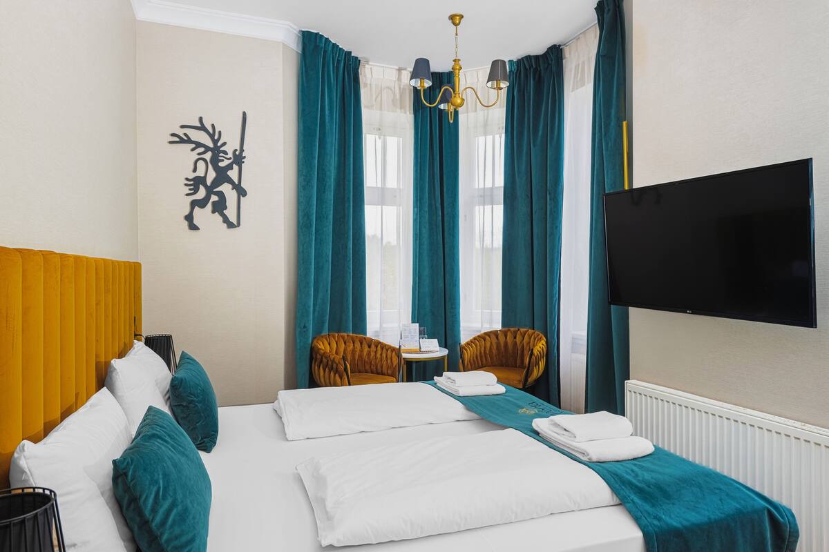 Quarto de hotel com uma cama, duas cadeiras, uma televisão e uma janela com cortinas.