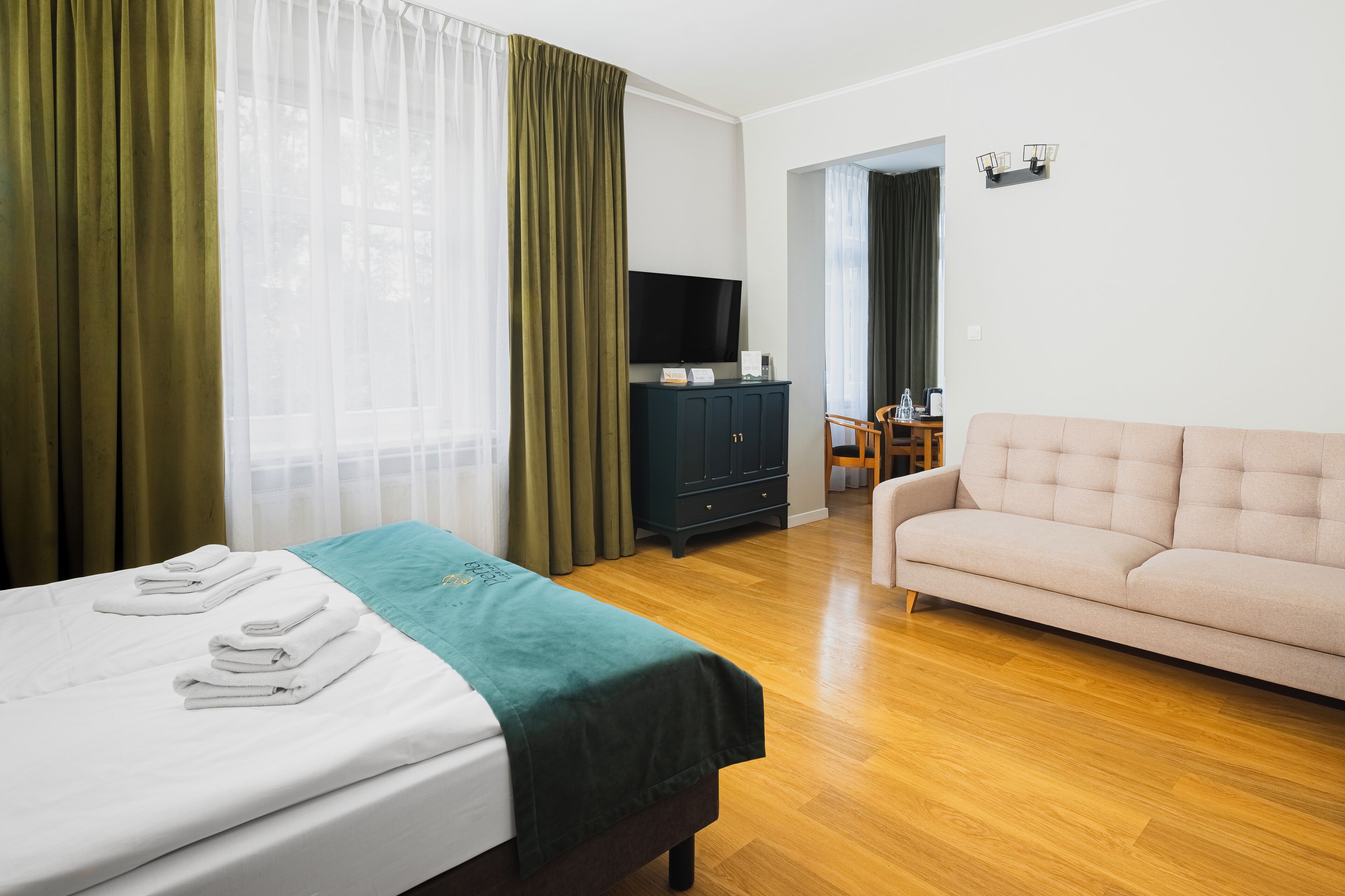 A hotel room with a bed, a sofa, a TV, and a wooden floor.