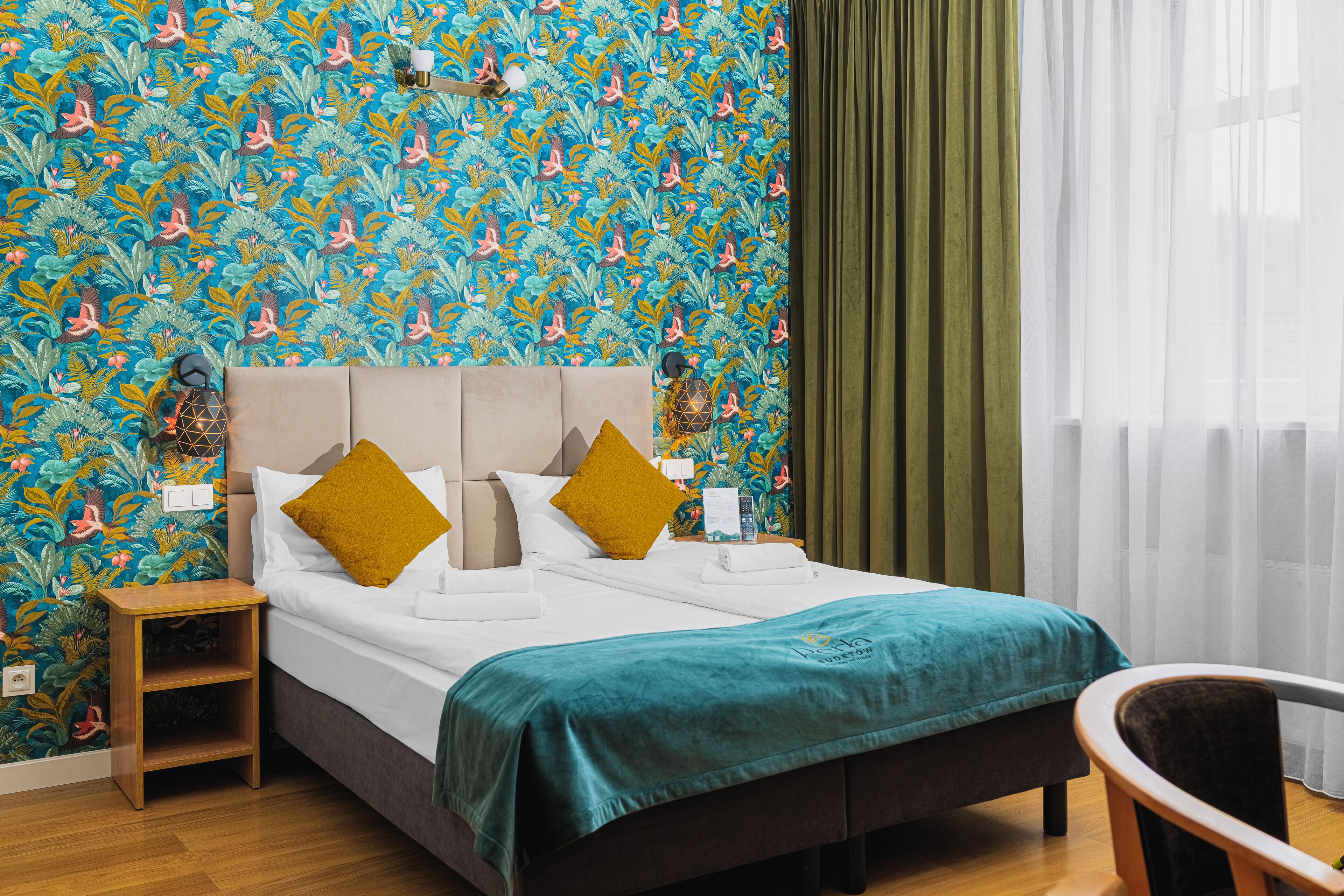 A hotel room with a bed, a nightstand, a chair, and a window with curtains.