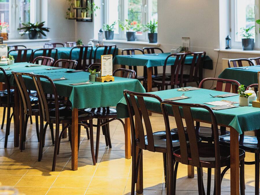 Un restaurante con varias mesas y sillas, ventanas amplias y plantas en macetas.
