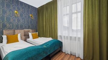 Une chambre d’hôtel avec deux lits, un mur décoré d’un motif et une grande fenêtre avec des rideaux légers.